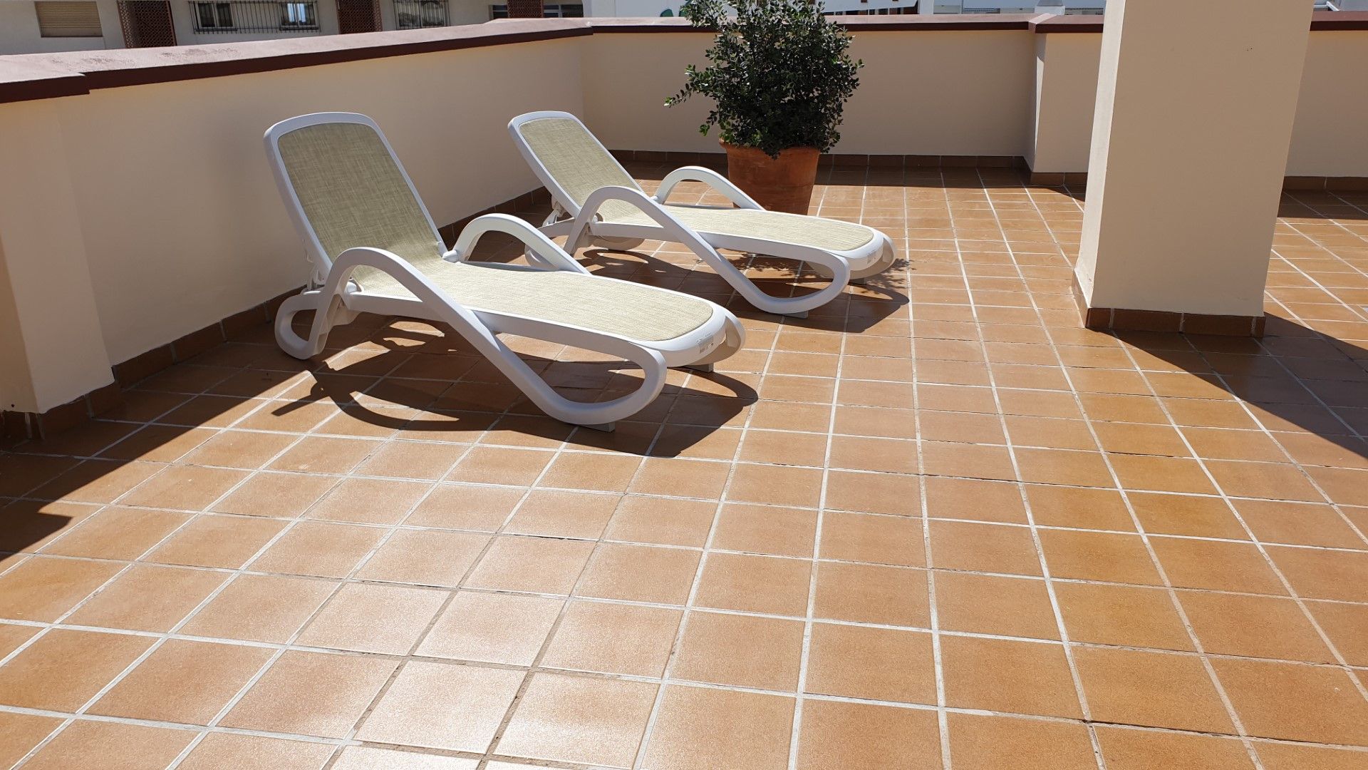 Zwei weiße Lounge-Sessel mit gepolsterten Sitzen und Lehnen, auf einer gefliesten Terrasse mit einem Blumentopf in der Nähe.
