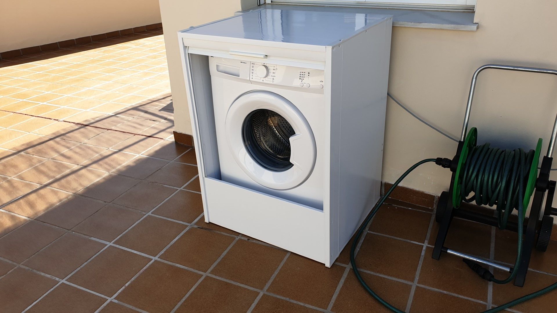 Eine Waschmaschine mit Frontlader und einem Schlauch, der an einem Metallständer befestigt ist.