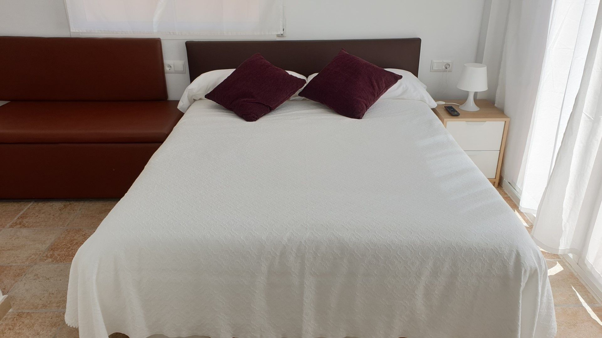 A hotel room with a bed, a nightstand, a lamp, and a brown sofa.