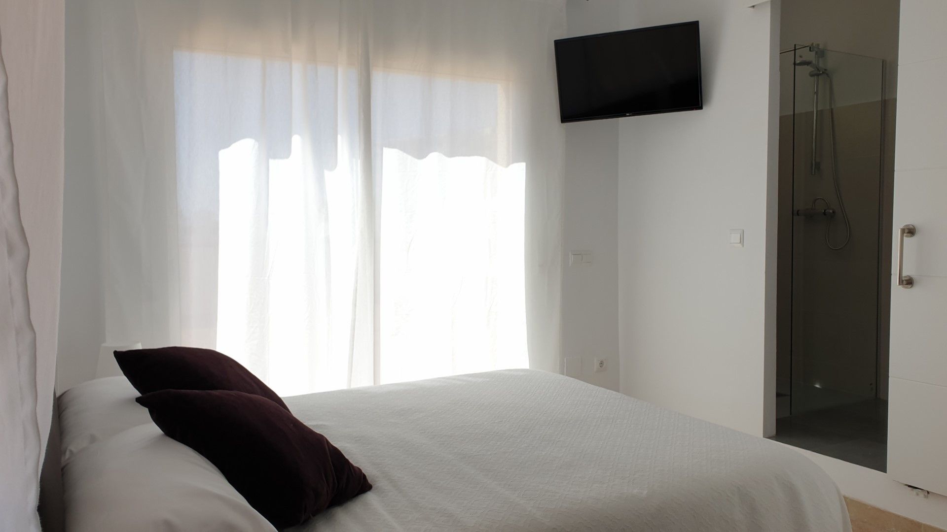 Ein Schlafzimmer mit einem Bett, einem an der Wand befestigten Fernseher und einem Duschbereich.