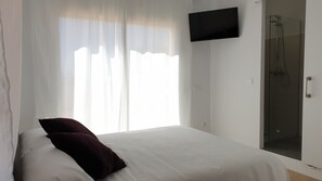 Ein Schlafzimmer mit einem Bett, einem an der Wand befestigten Fernseher und einem Duschbereich.