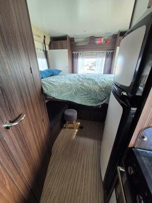 Un intérieur de camping-car compact comprenant un lit, un coin cuisine et un petit tabouret.