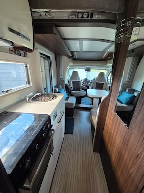 A compact RV interior with a kitchenette, seating area, and a small table. - Amazing self contained motor home. Stays parked. Close to all city amenities. (Palmerston North)