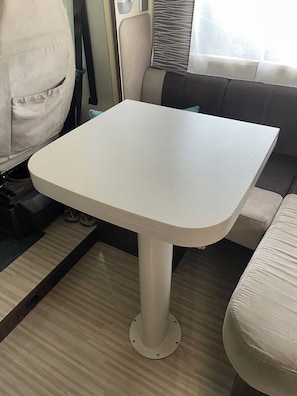 A white table in a room with a sofa and a window with curtains. - Amazing self contained motor home. Stays parked. Close to all city amenities. (Palmerston North)