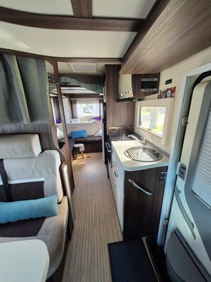 Un intérieur de camping-car compact comprenant un coin cuisine, un espace repas et un coin nuit.