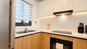 A modern kitchen with a double sink, wooden cabinets, a black range hood, and a window with blinds. - Born | 2 bedrooms with pool views (Bávaro)