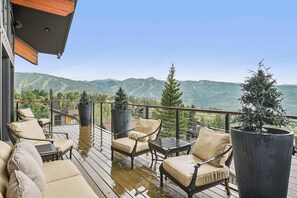 Eine Terrasse mit Gartenmöbeln und Topfpflanzen, mit Blick auf eine gebirgige Landschaft.