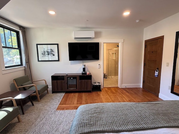 A modern bedroom with a bed, a TV, a desk, and a shower area. - The Crescent Hotel (Crescent Mills)