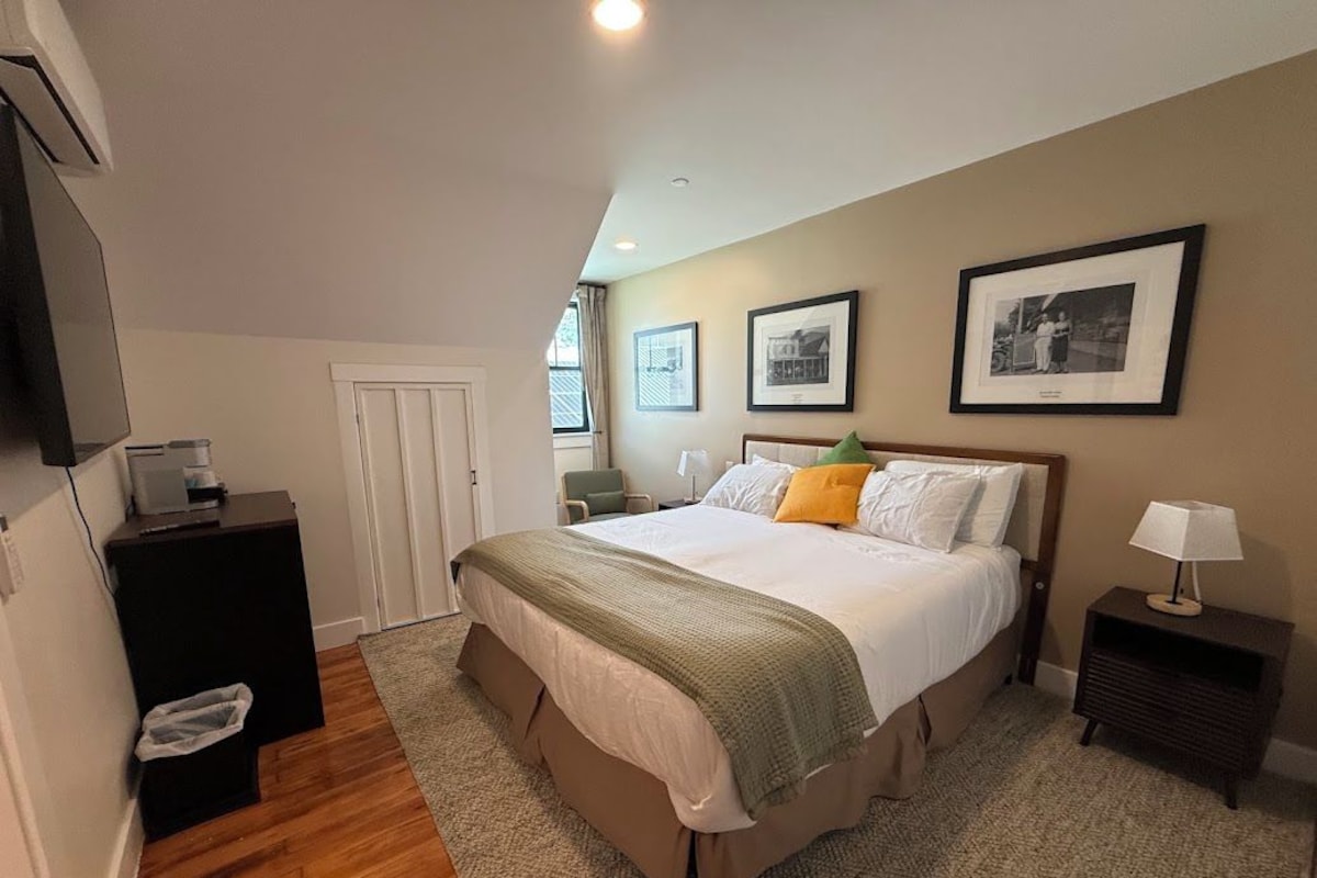 A bedroom with a bed, bedside tables, a lamp, framed pictures on the wall, and a door.