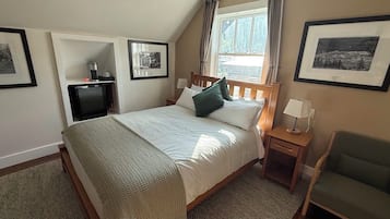 A bedroom with a bed, bedside tables, a chair, a television, and framed pictures on the walls.