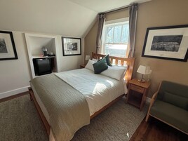 Un dormitorio con cama, mesitas de noche, una silla, un televisor y cuadros en las paredes.
