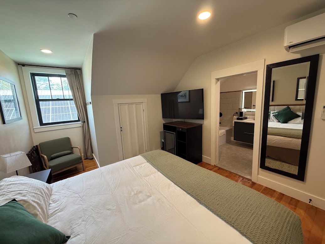 Un dormitorio con cama, escritorio, silla, televisor y espejo.