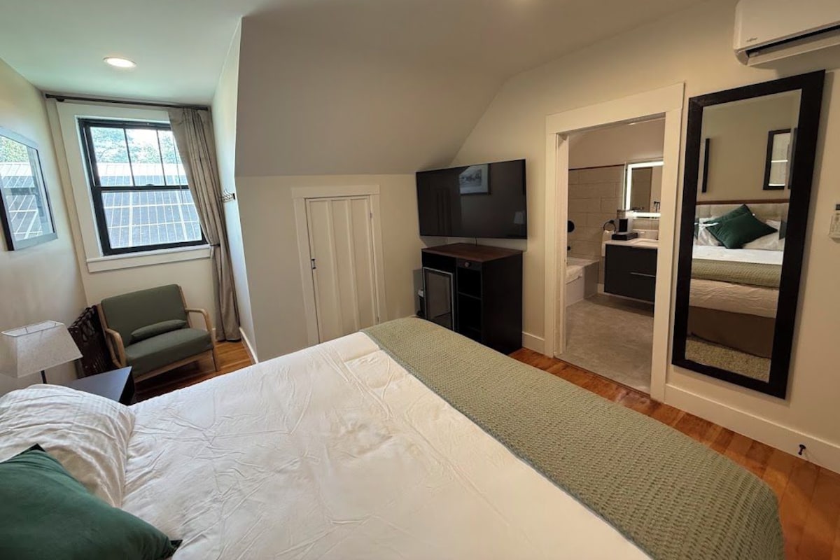 A bedroom with a bed, a desk, a chair, a television, and a mirror.
