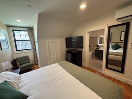 Un dormitorio con cama, escritorio, silla, televisor y espejo.