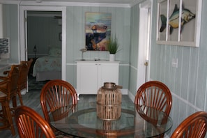 A dining area with a glass table surrounded by wooden chairs, a white cabinet with a painting above it, and a door leading to another room. - Lovely Waterfront Cottage #1821, private patio, overlooking river. Ruskin, FL (Ruskin)