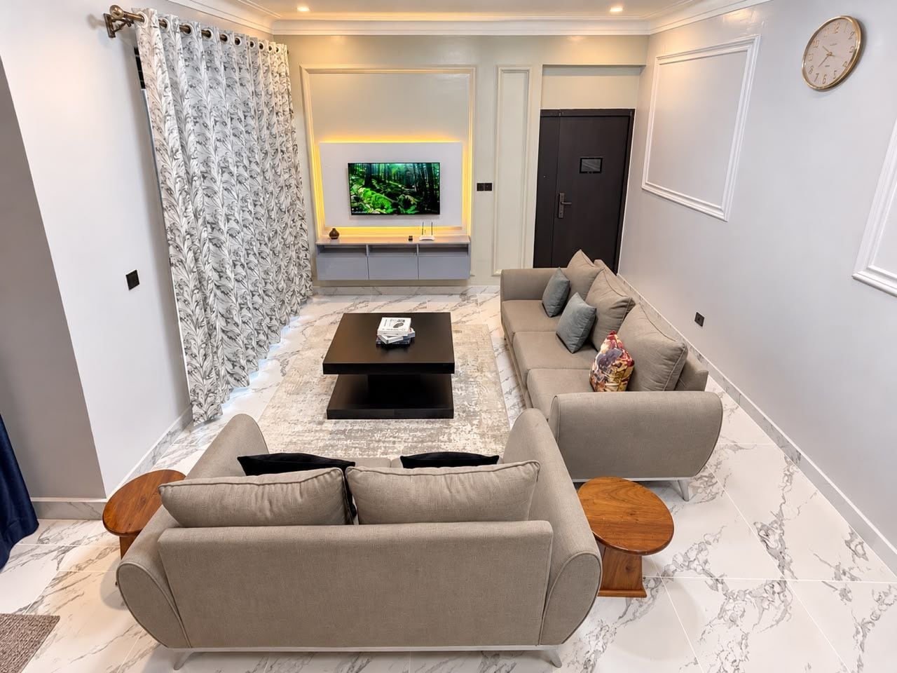 A modern living room with a flat-screen TV, a sofa set, a coffee table, and a patterned curtain.