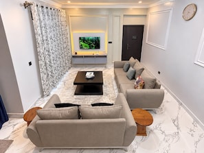Una sala moderna con televisor de pantalla plana, un conjunto de sofá, una mesa de centro y una cortina estampada.