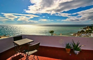 A balcony with a table and chairs, overlooking a coastal view with the sea and a clear sky. - Carabeo 78X-2 (Nerja)
