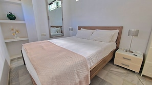 A neatly made bed with a wooden headboard, a bedside table with a lamp, and a mirror on the wall. - Carabeo 78X-2 (Nerja)