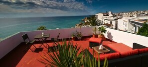 A terrace with outdoor seating, a view of the sea, and white buildings in the background. - Carabeo 78X-2 (Nerja)