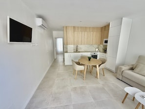 A modern kitchen with a dining area, a TV mounted on the wall, and a sofa in the living space. - .Bajo A (Nerja)