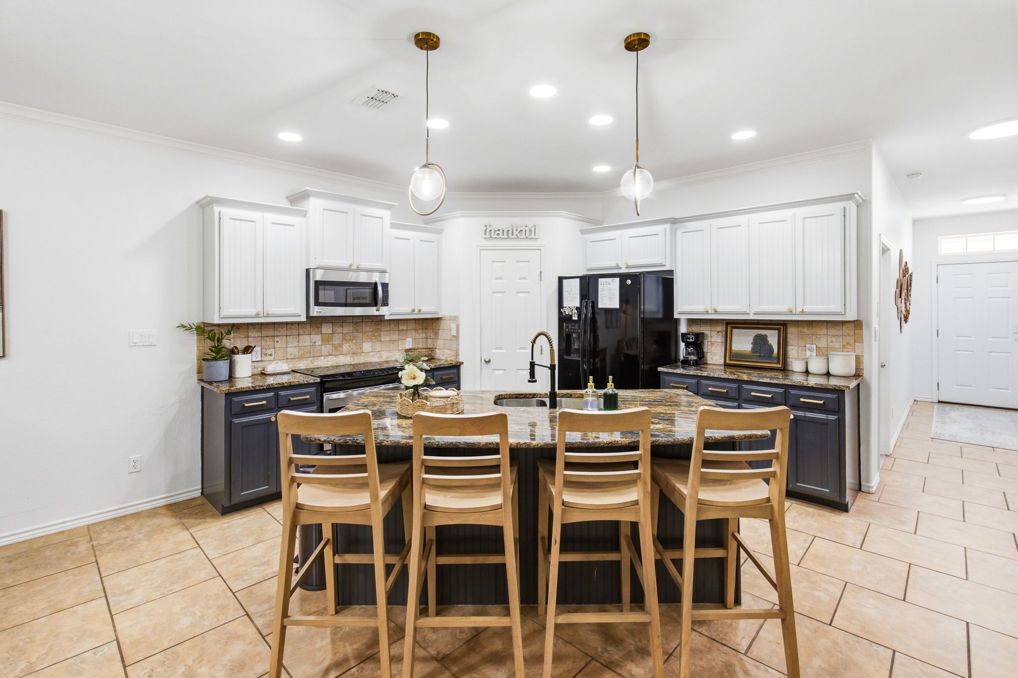 Una cocina moderna con armarios blancos, una isla central con taburetes de bar, electrodomésticos de acero inoxidable e iluminación colgante.