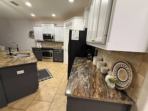A modern kitchen with granite countertops, a built-in oven, and white cabinetry. - Private Boat Dock + Beach Access | Canal-Front (Corpus Christi)