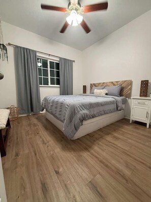 A bedroom with a bed, a nightstand, a ceiling fan, and a window with curtains. - Private Boat Dock + Beach Access | Canal-Front (Corpus Christi)