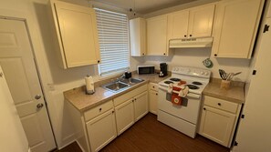 A compact kitchen with white cabinets, a microwave, a stove, and a sink. - Portifino-Cozy on Charles (Montgomery)