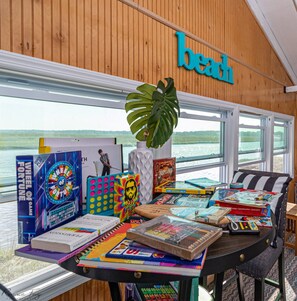 Ein Zimmer mit Blick auf ein Gewässer, ein Tisch mit Büchern und Spielen sowie ein Schild mit der Aufschrift 'beach'.