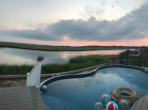 Ein Schwimmbad mit Blick auf einen See und einen Sonnenuntergang.