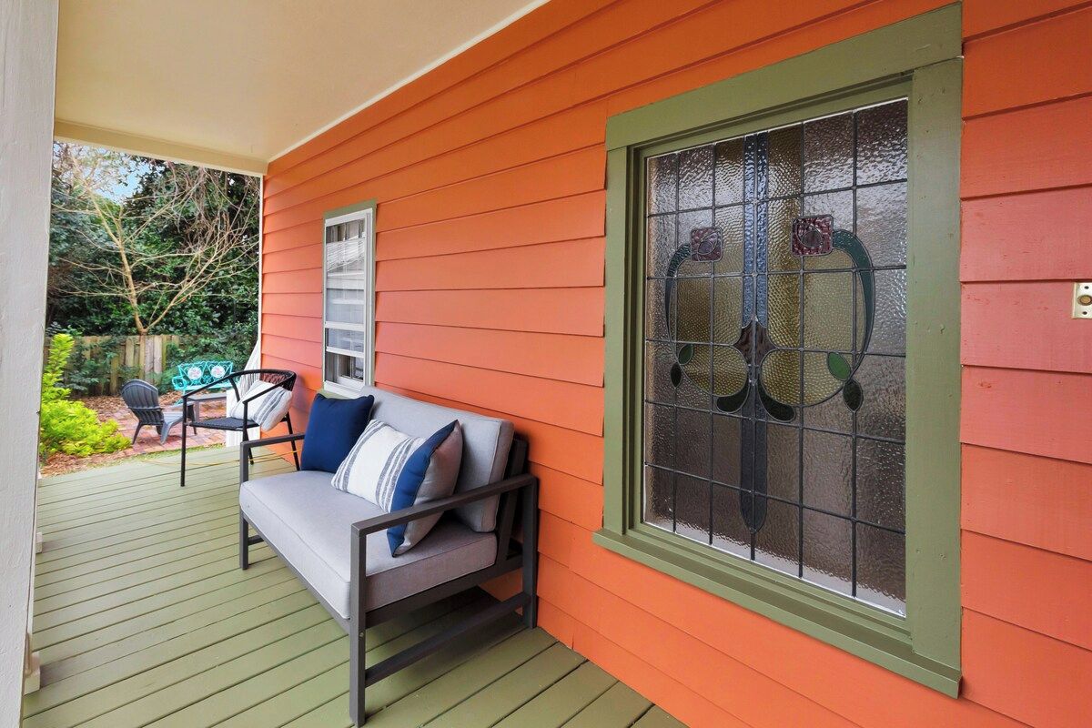 A porch with a green bench, a window with decorative glass, and a view of a garden.