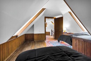 Ein Schlafzimmer mit schrägem Dach, Holzwänden, einem Bett mit schwarzer Bettdecke und einem farbenfrohen Teppich.