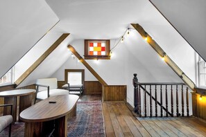 Ein Loft-Zimmer mit einer Holztreppe, einem kleinen Fenster mit Schachbrettmuster und Lichterketten.