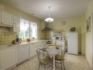 A kitchen with white cabinets, a dining table with chairs, a microwave, and a refrigerator. - Cosy gîte with garden, pets allowed (Commelle-Vernay)