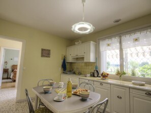 A kitchen with a dining table set for two, a window with a view, and a hanging light fixture. - Cosy gîte with garden, pets allowed (Commelle-Vernay)