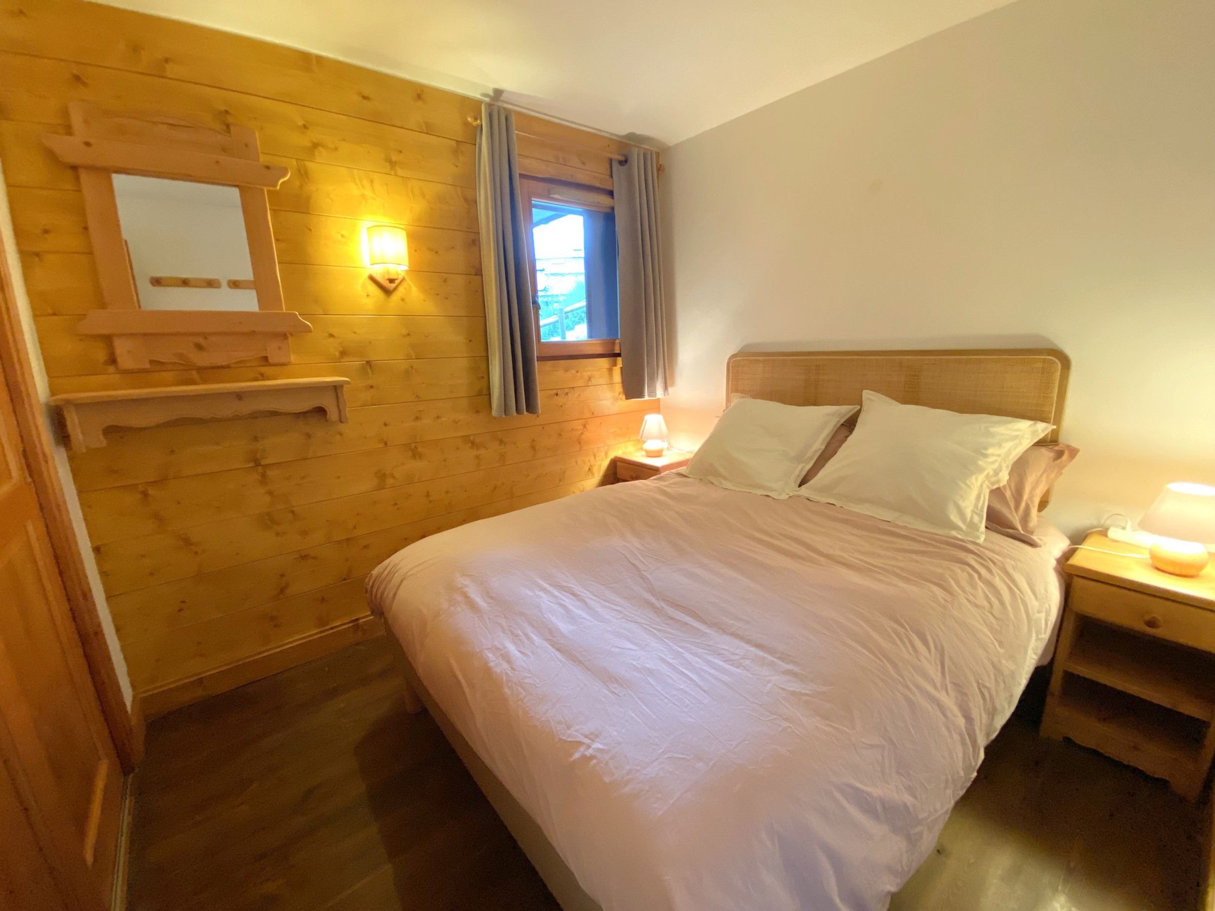 Une pièce avec un mur en bois, un lit avec une literie blanche, une table de chevet avec une lampe et une fenêtre avec des rideaux.