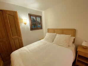 A bedroom with a bed, a wooden door, a wall-mounted picture, and a bedside table with a lamp. - Renovated apartment, mountain view - 4 guests (Méribel)
