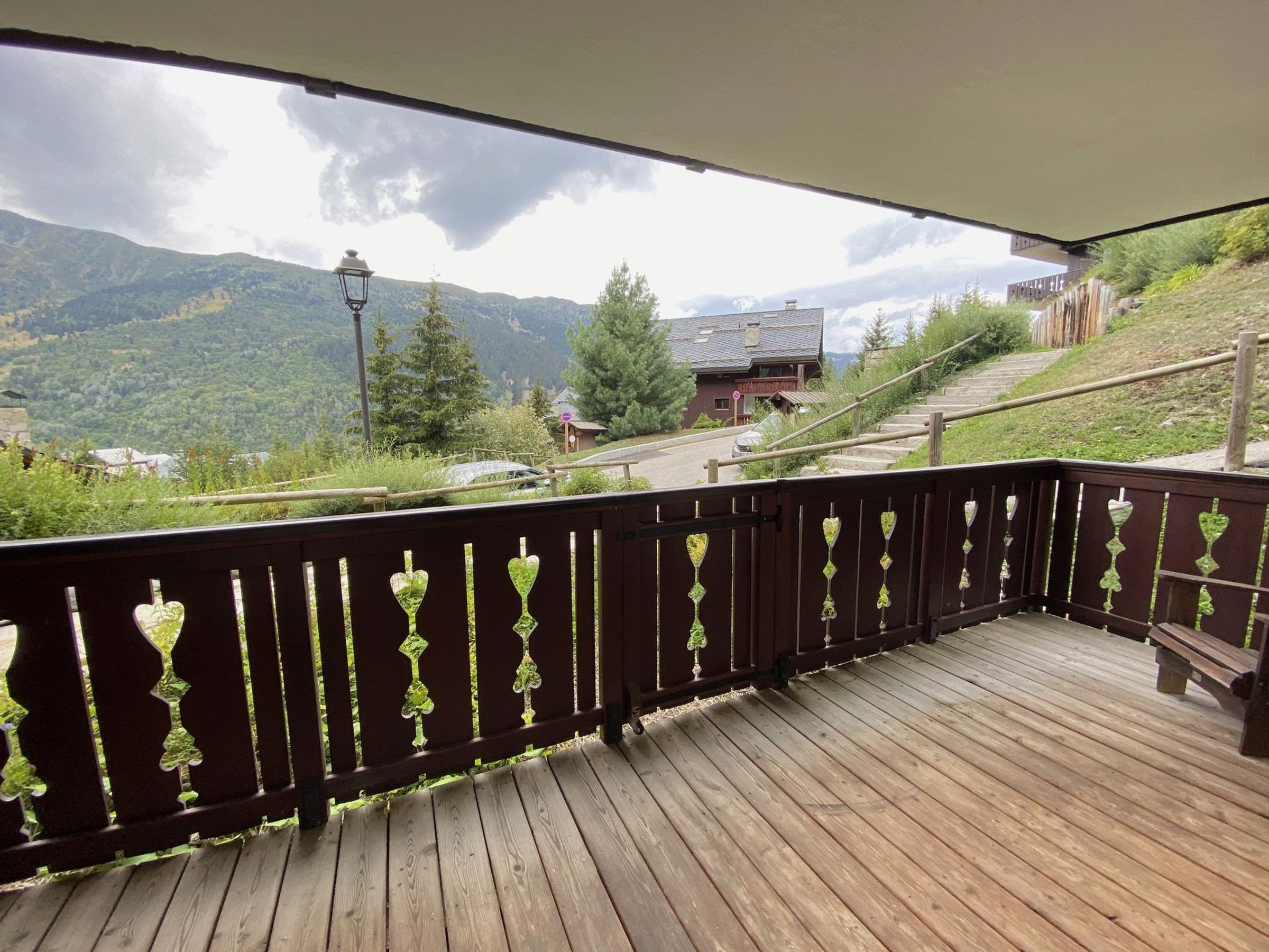 A wooden deck with a railing, overlooking a mountainous landscape with a road and buildings.