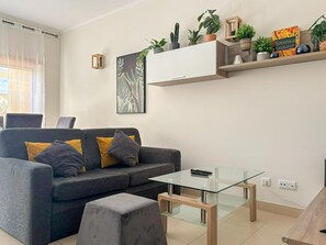 A modern living room with a sofa, a glass coffee table, and a wooden side table. - Apartment with balcony pool access - 4 guests (Tavira)