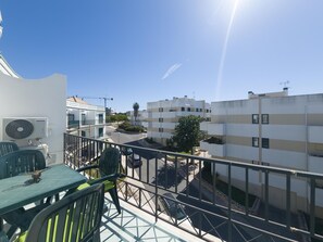 Een balkon met een tafel en stoelen, met uitzicht op een woonwijk met meerdere gebouwen en een heldere lucht.