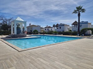 A swimming pool with a wooden deck, a lifeguard tower, and villas in the background. - Charming studio, relax in Cabanas (Tavira)