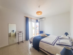 A bedroom with a bed, a bedside table, a lamp, a hanging light fixture, a mirror, and a window with curtains. - Villa with air conditioning in Altura - 6 guests (Altura)