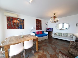Ein Wohnzimmer mit Esstisch, Sofa, Fernseher und Kunstwerken an den Wänden.