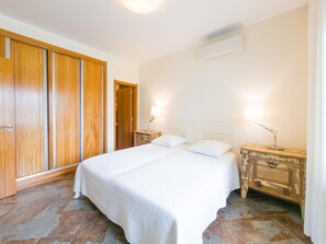 Quarto com cama, mesas de cabeceira, ar condicionado e guarda-roupa.