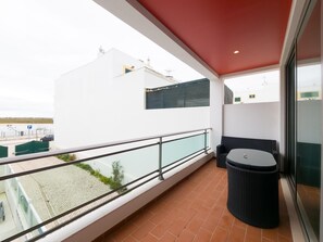 A balcony with a glass railing, a wicker chair, and a trash bin. - Eclectic apartment in the heart of Cabanas - 3 guests (Tavira)