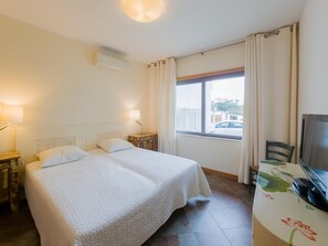 A hotel room with a bed, bedside lamps, a TV, and a window with curtains. - Eclectic apartment in the heart of Cabanas - 3 guests (Tavira)