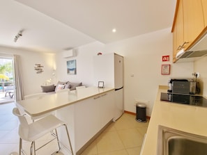 A modern kitchen with a central island, bar stools, a refrigerator, and a trash bin. - Modern apartment near Ria Formosa (Tavira)