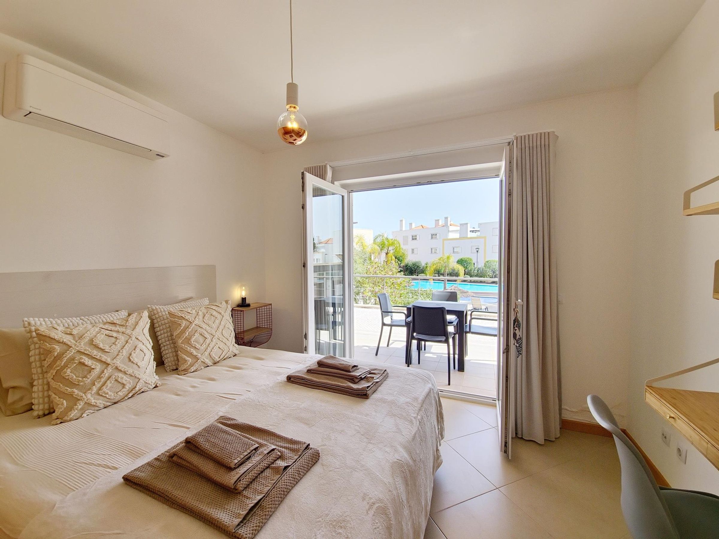 Un dormitorio con cama, mesitas de noche, lámpara y vistas a un área de piscina exterior.