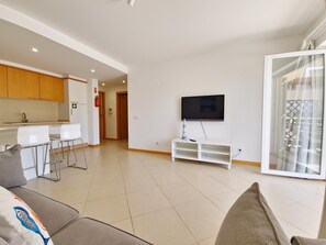 A spacious living area with a kitchen, a flat-screen TV mounted on the wall, and a sliding glass door leading to a balcony. - Modern apartment near Ria Formosa (Tavira)